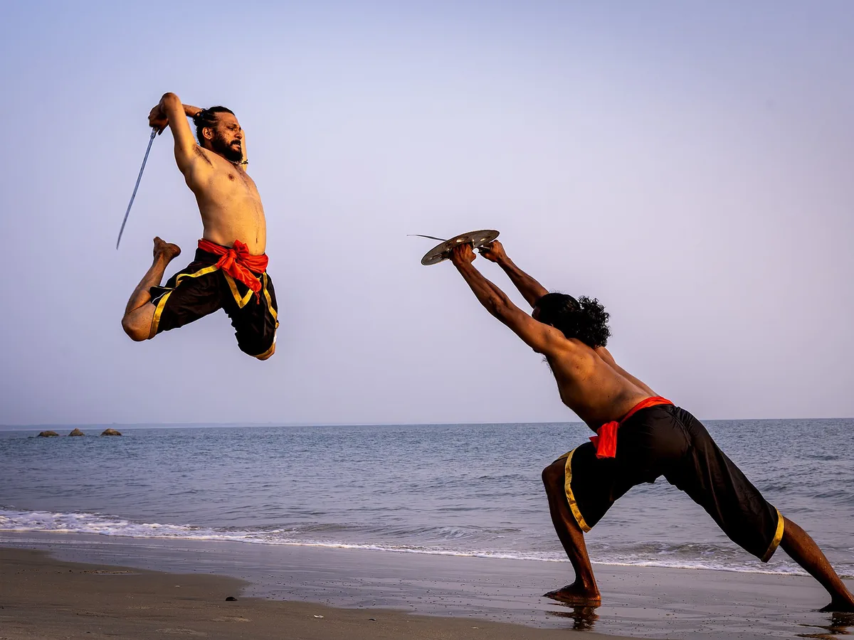 A Kalaripayattu practitioner defending with a traditional shield and sword on a Kerala beach